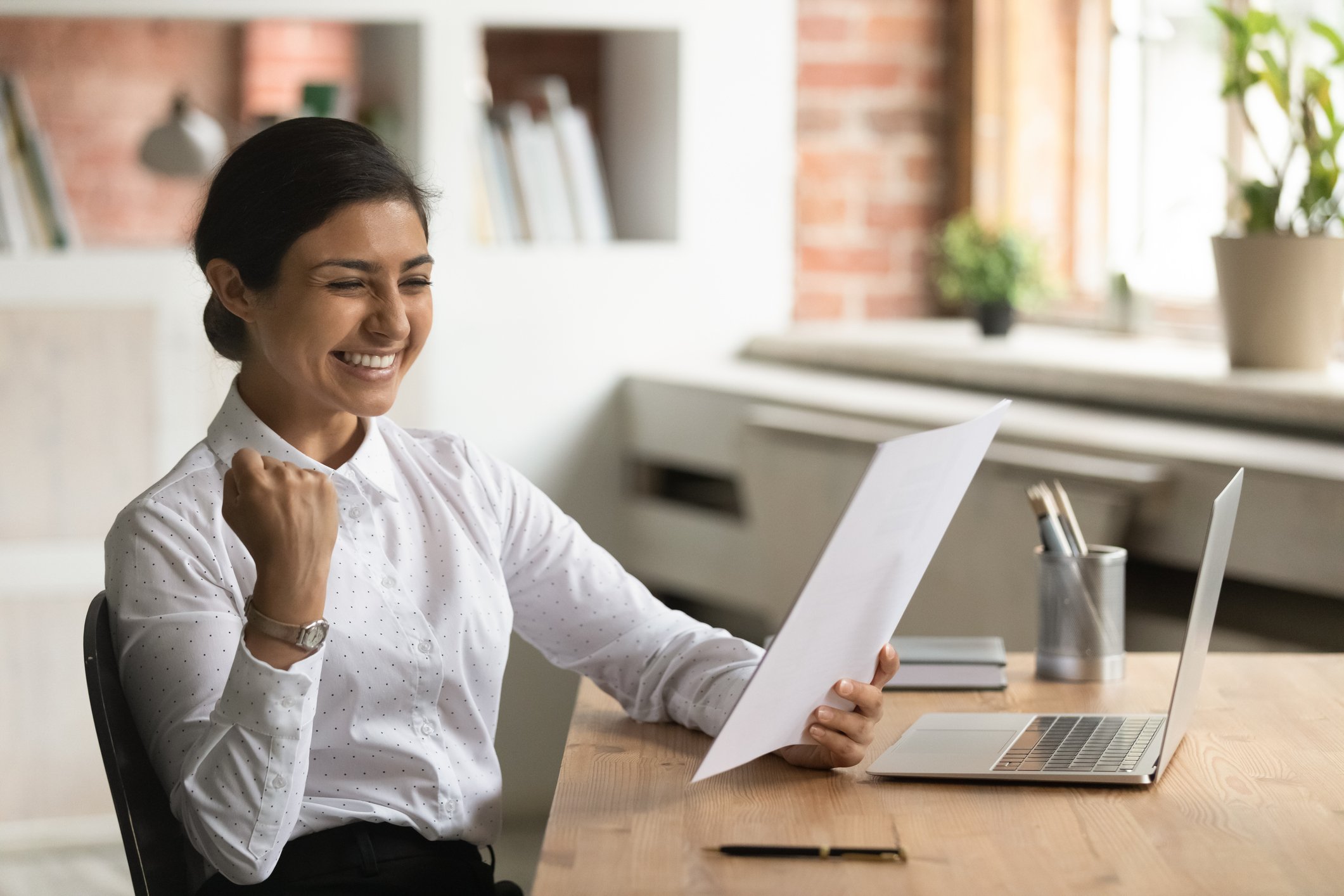 A smiling person pumps their fist in celebration, reading a document in the other hand.