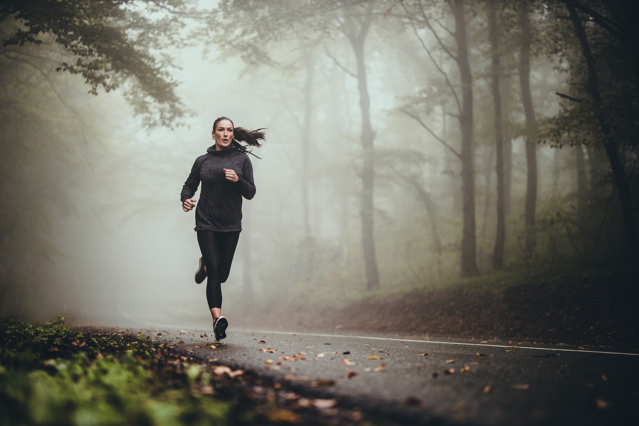 Jogger running along a foggy forest road.