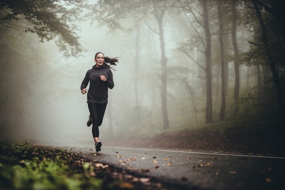 Jogger running along a foggy forest road.