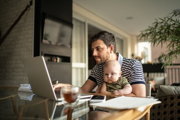 A person sitting with a baby while also on the computer.