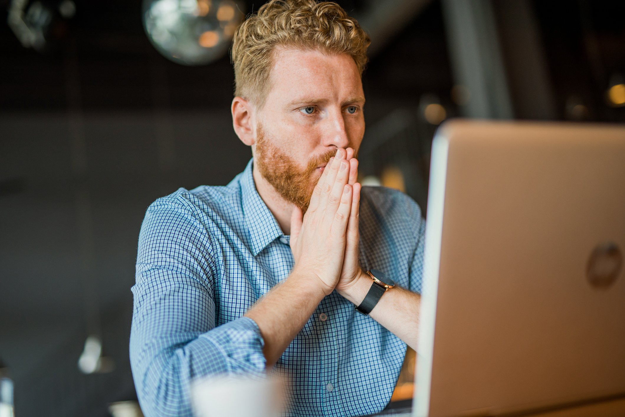Person with hands pressed together in front of their face is looking at a laptop screen.