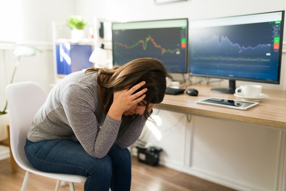 Person with head in hands seated at desk bearing two monitors displaying graphs.
