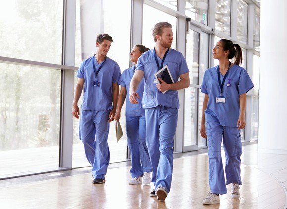 Medical personal walk down a hallway with large windows in the background