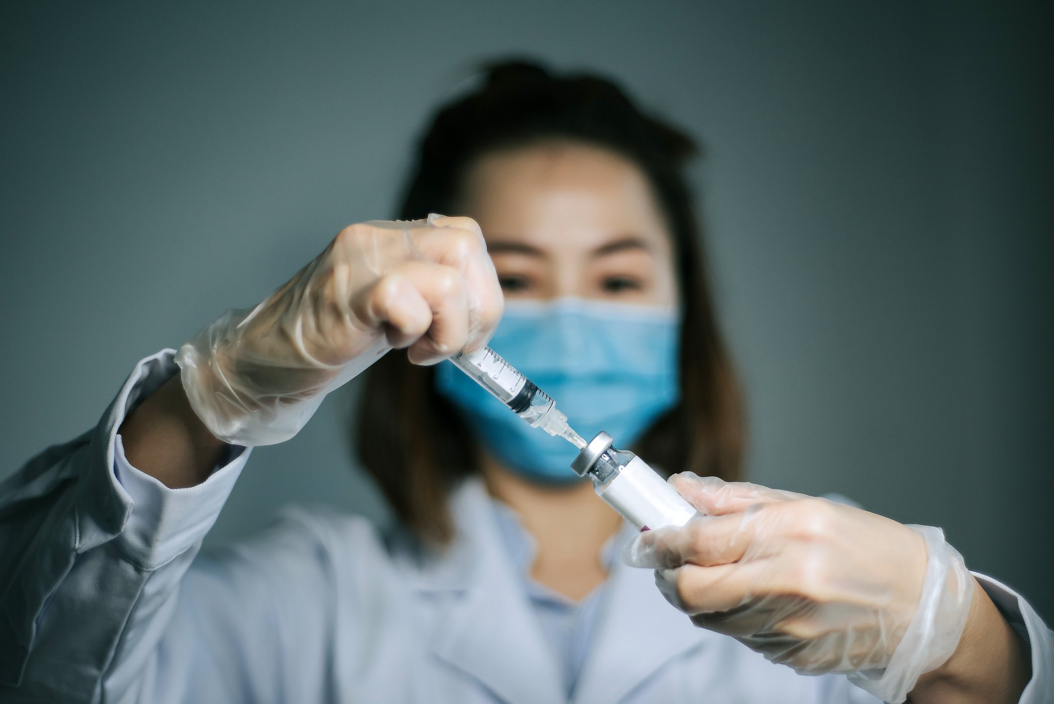 A healthcare professional holding a syringe with needle inserted into a vaccine vial.