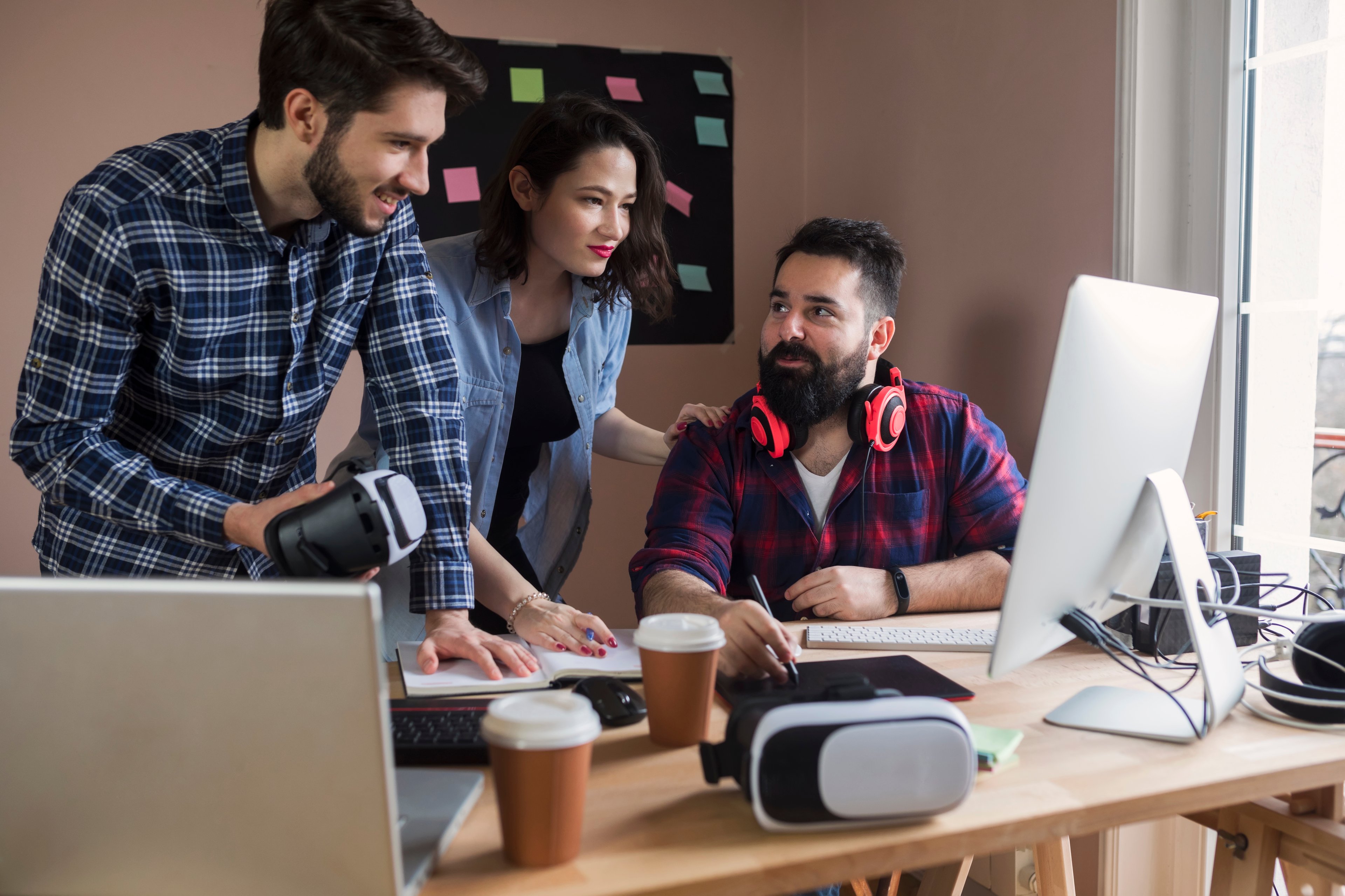 Three people in an office holding VR headsets gathered around a computer.