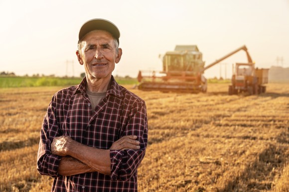 A person standing in a field, with farm equipment working behind.