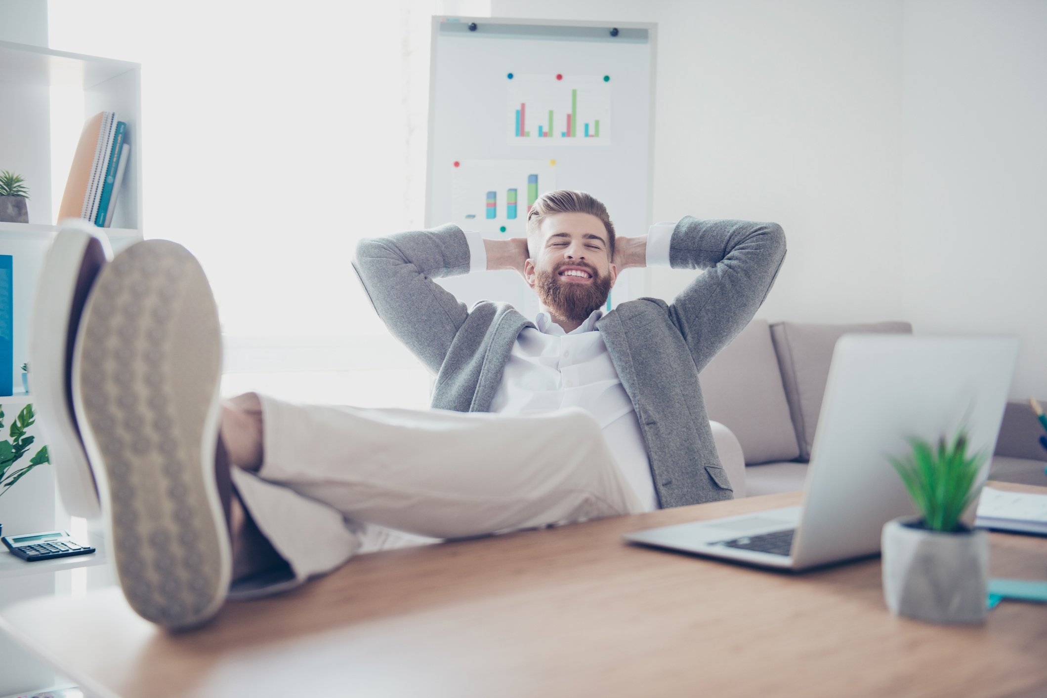 An investor smiles with satisfaction as leans back in his chair, his feet kicked up on his desk.