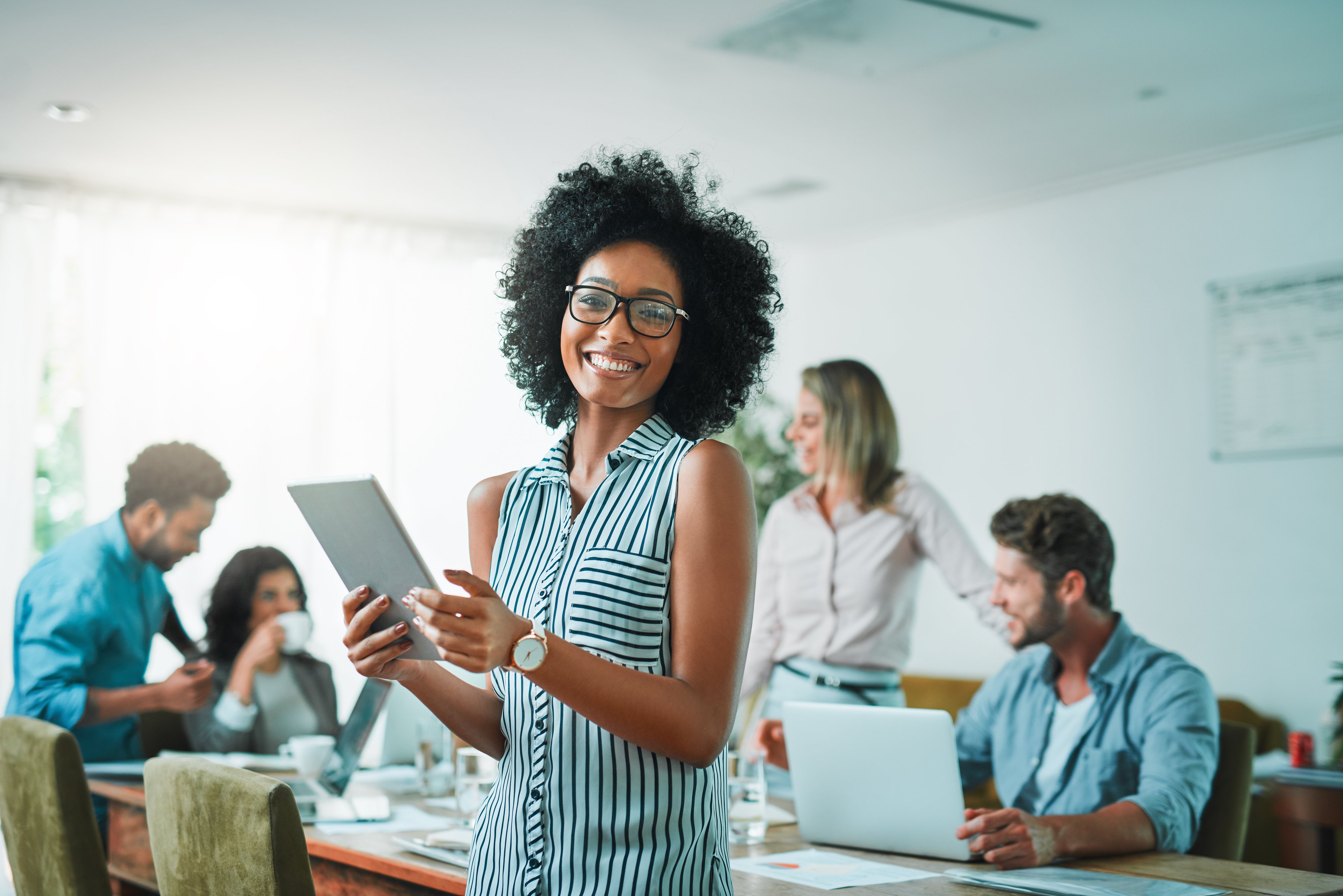 Someone smiling while holding a tablet in an office setting.