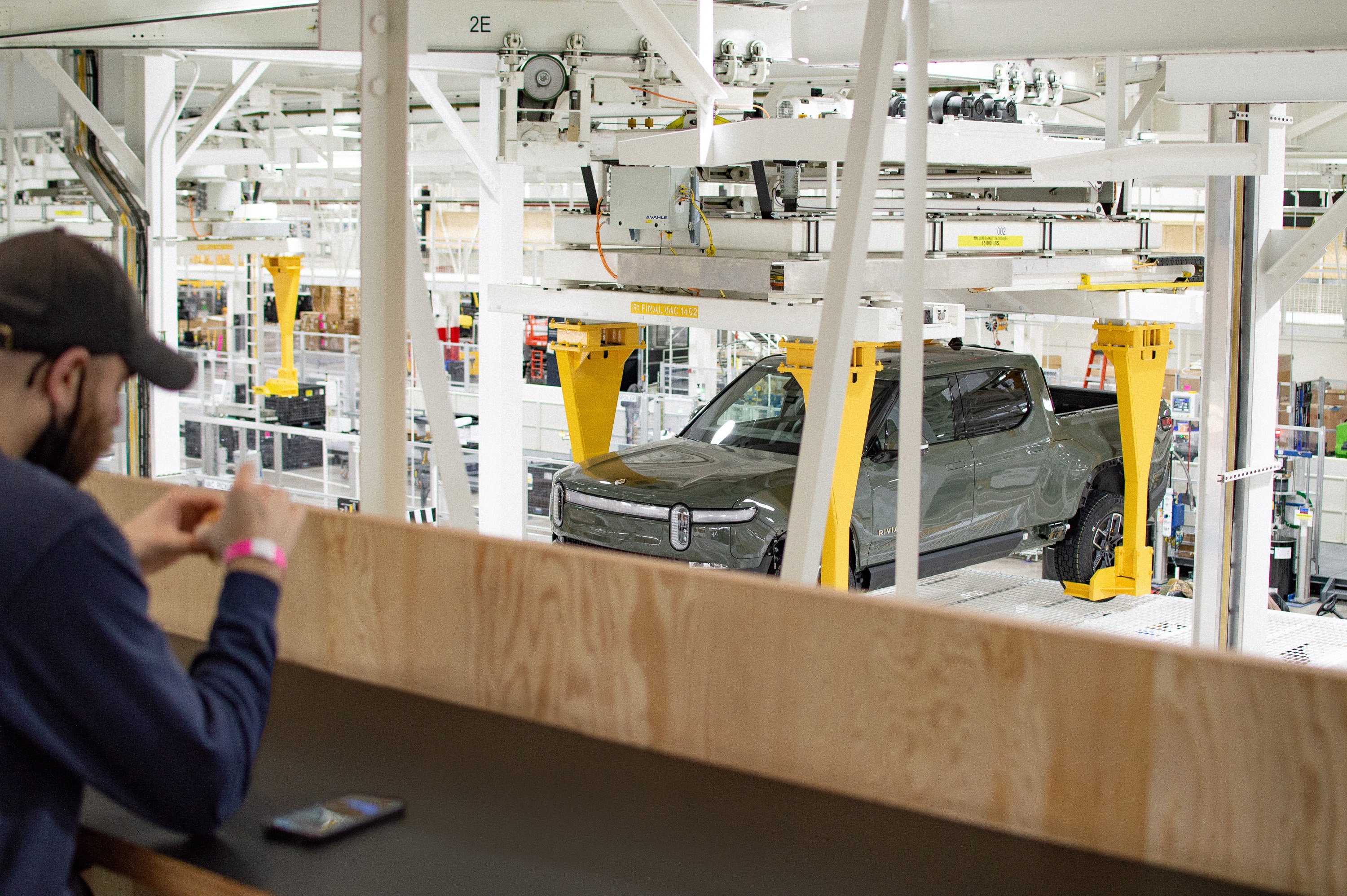 Worker at Rivian production facility with R1T electric pickup truck. 