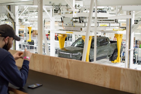 Worker at Rivian production facility with R1T electric pickup truck. 