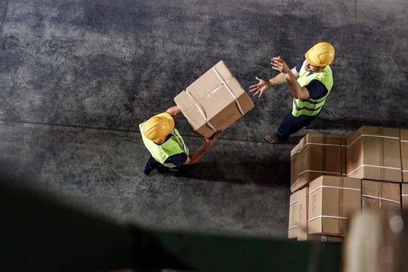 Overhead view of two warehouse workers passing a box.