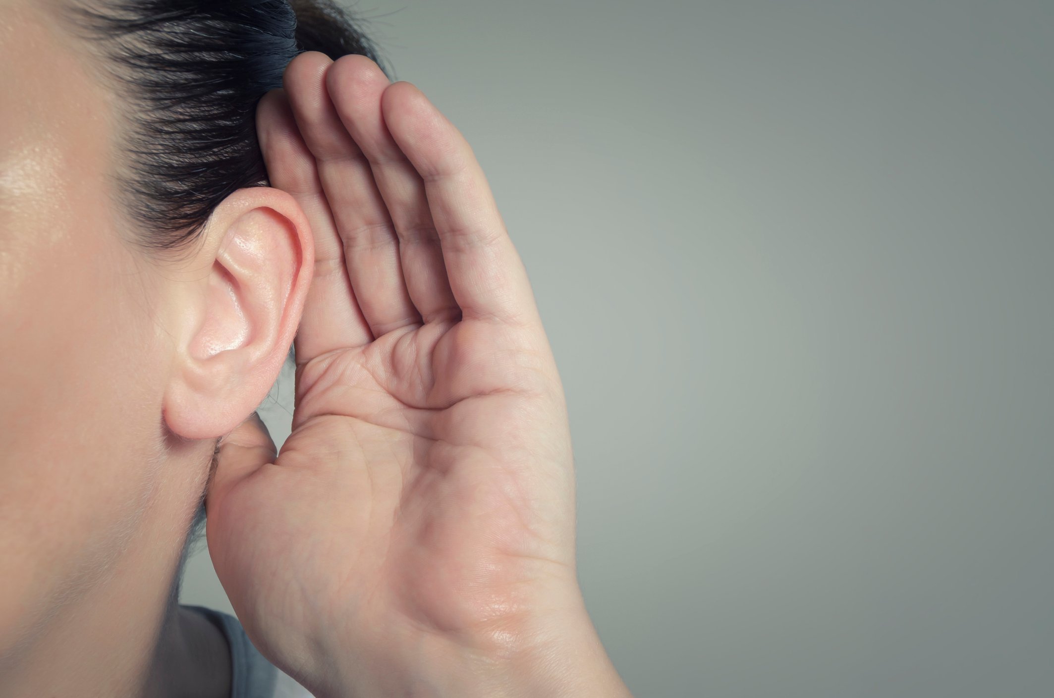 Person with their hand cupped over their ear listening for a quiet sound.