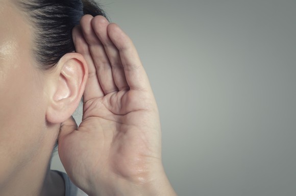 Person with their hand cupped over their ear listening for a quiet sound.