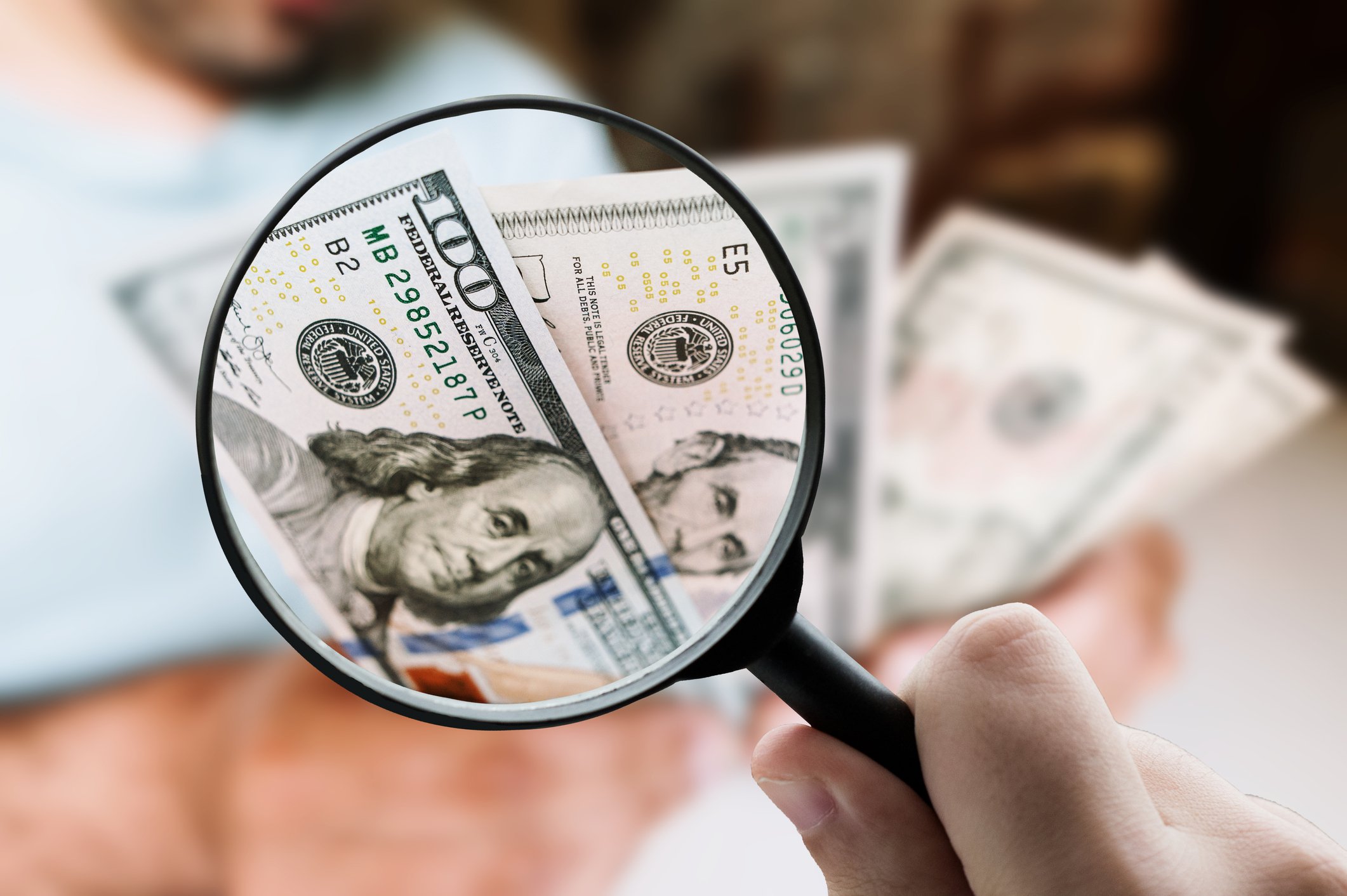 A magnifying glass hovering over a $100 bill.