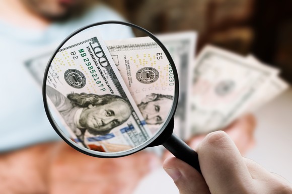 A magnifying glass hovering over a $100 bill.