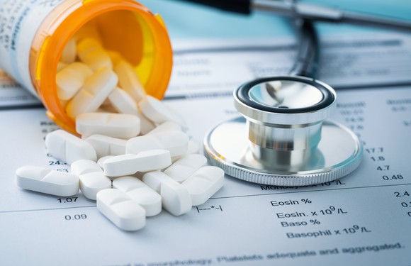 A vial of prescription medicine spills out onto a medical report, next to a stethoscope.