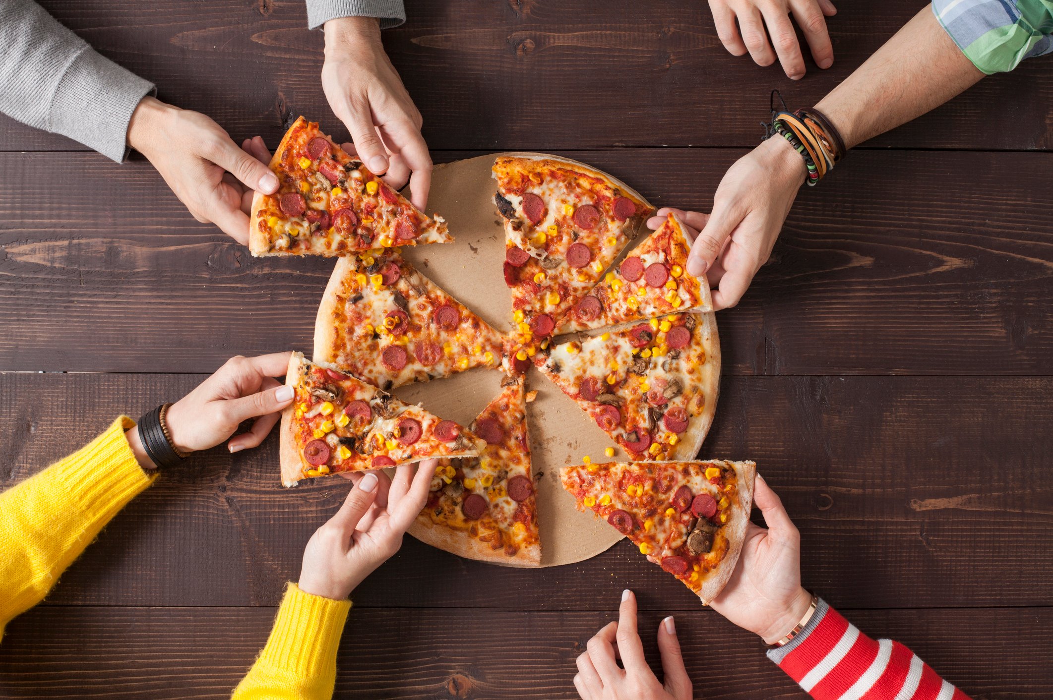 Group of people reaching for a slice of pizza.