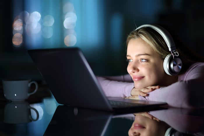 A young person wearing headphones watching media on a laptop.