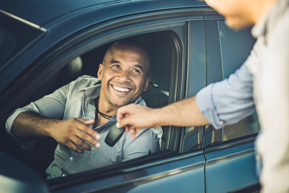 A person sitting in a car being handed the keys.