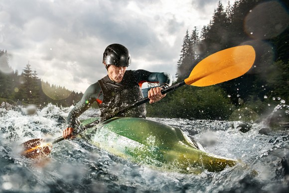 A person in a kayak rows through turbulent waters.