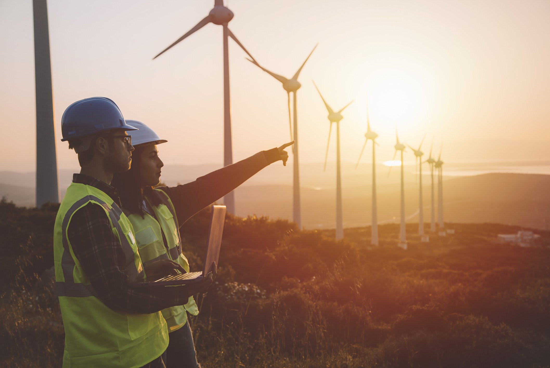 two workers stand in field with wind turbines