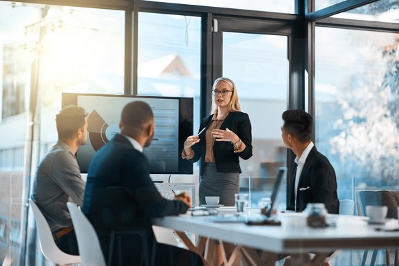 A professional gives a presentation to employees in a glass-walled conference room