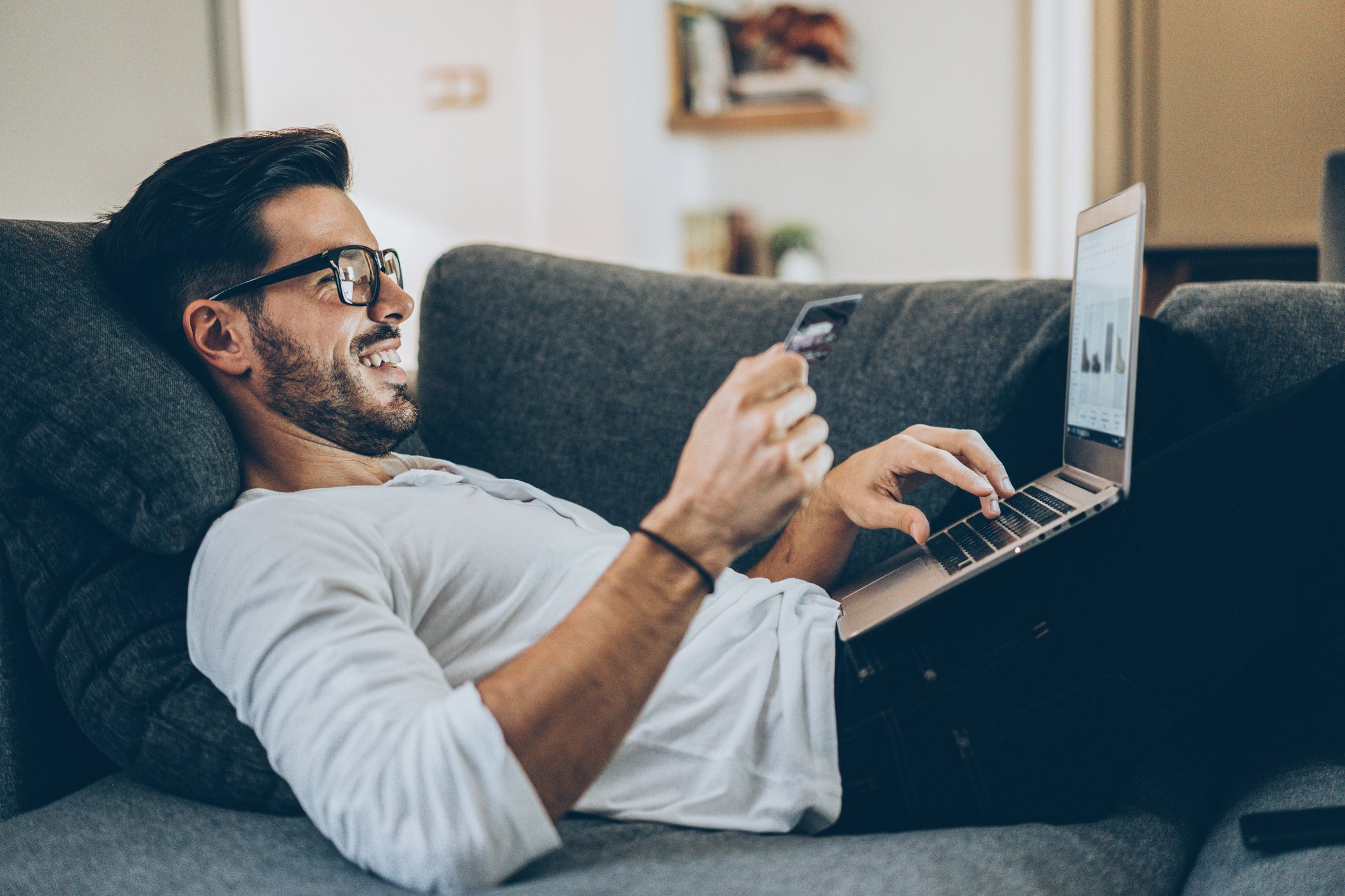 An individual relaxing on a couch smiles while shopping online.