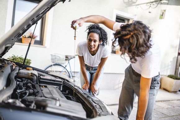 Two people check the oil in a car.