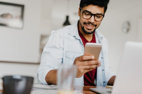 Person smiles while using phone and laptop.