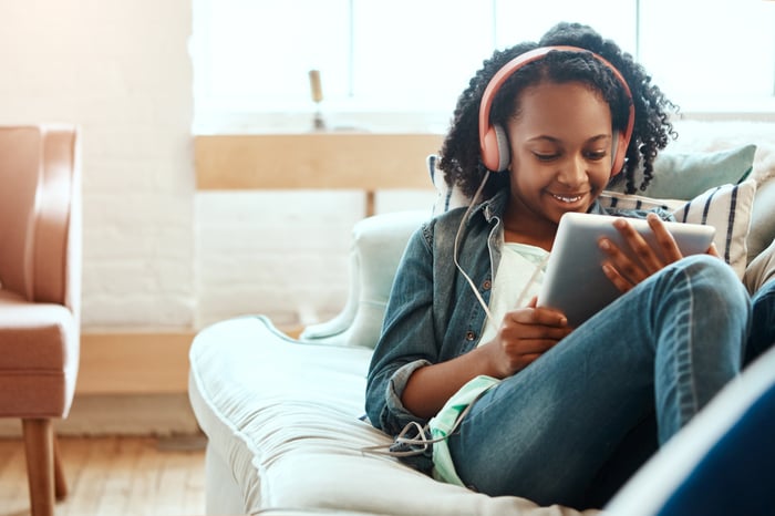 A person wearing headphones and looking at an electronic device.