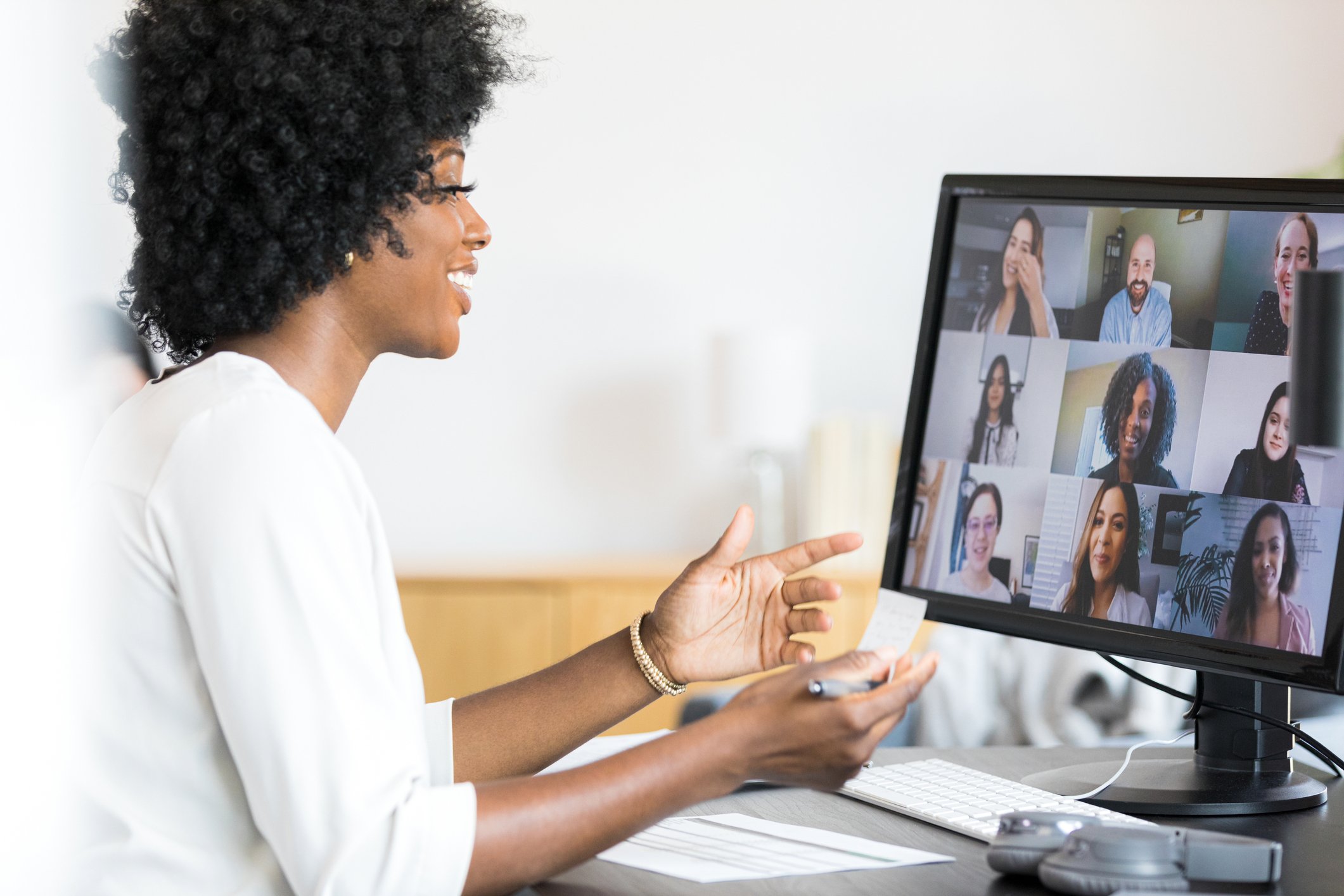 Person at a computer, smiling, with a screen showing a video conferece.