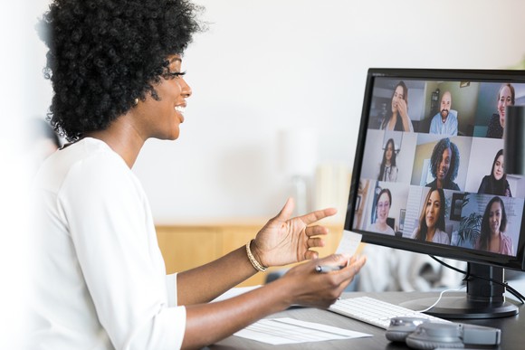 Person at a computer, smiling, with a screen showing a video conferece.