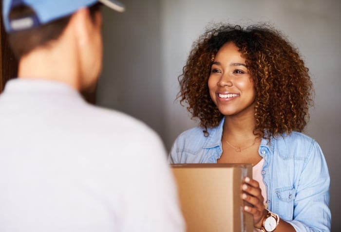 A smiling person receiving a package from a delivery person.
