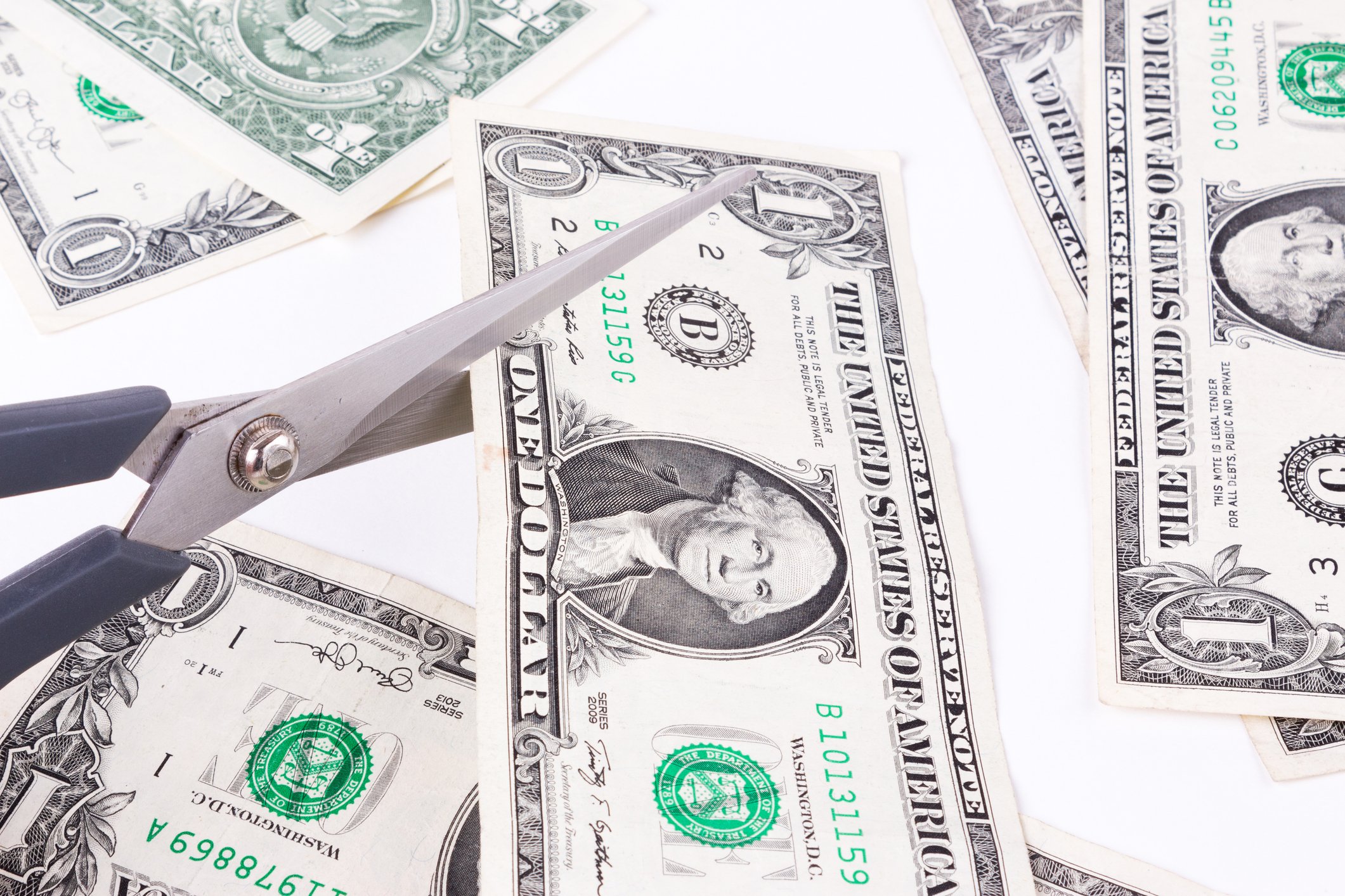 Scissors cutting dollar bills.