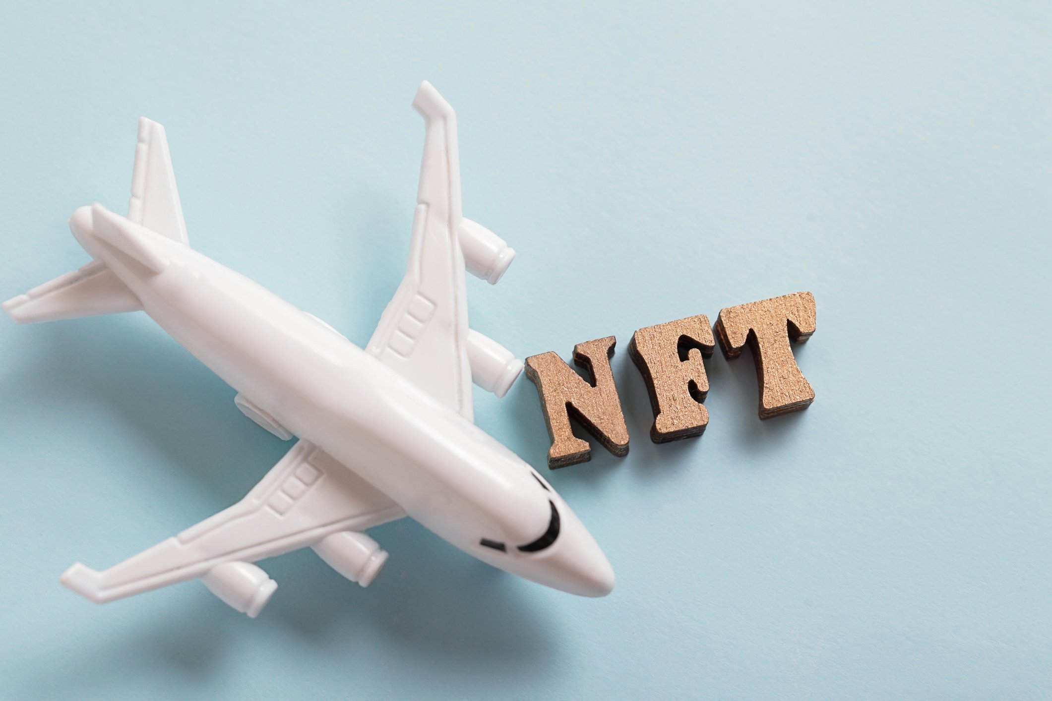 Model white airplane beside the letters NFT on a pale blue background.