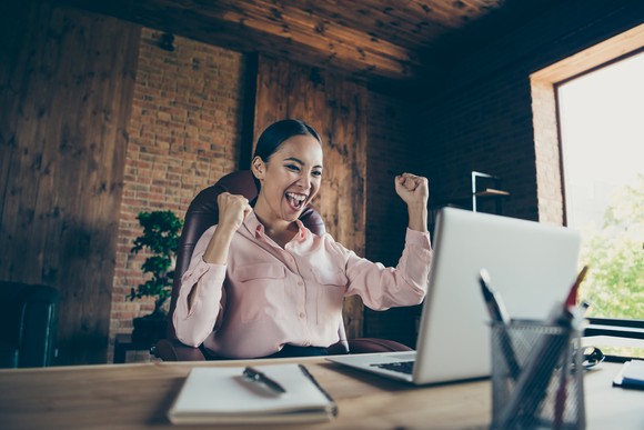 Happy investor cheering at a desk looking at a computer screen.