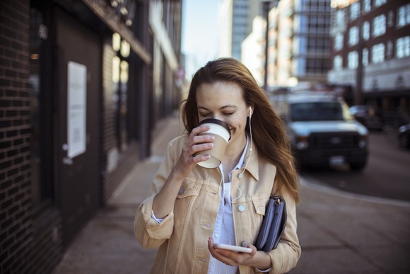 Person drinking coffee while walking and looking at phone.