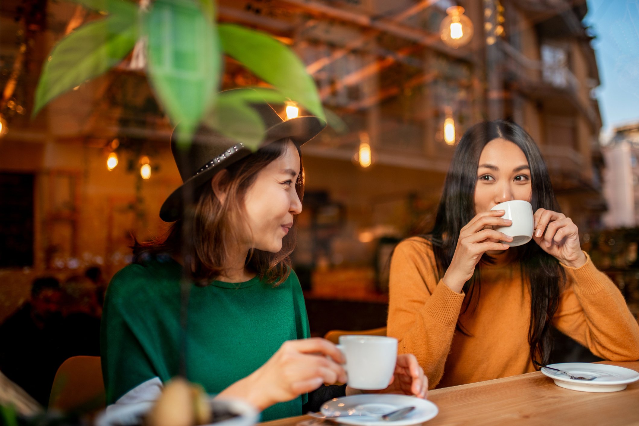 Two people drink out of coffee mugs in a cafe.