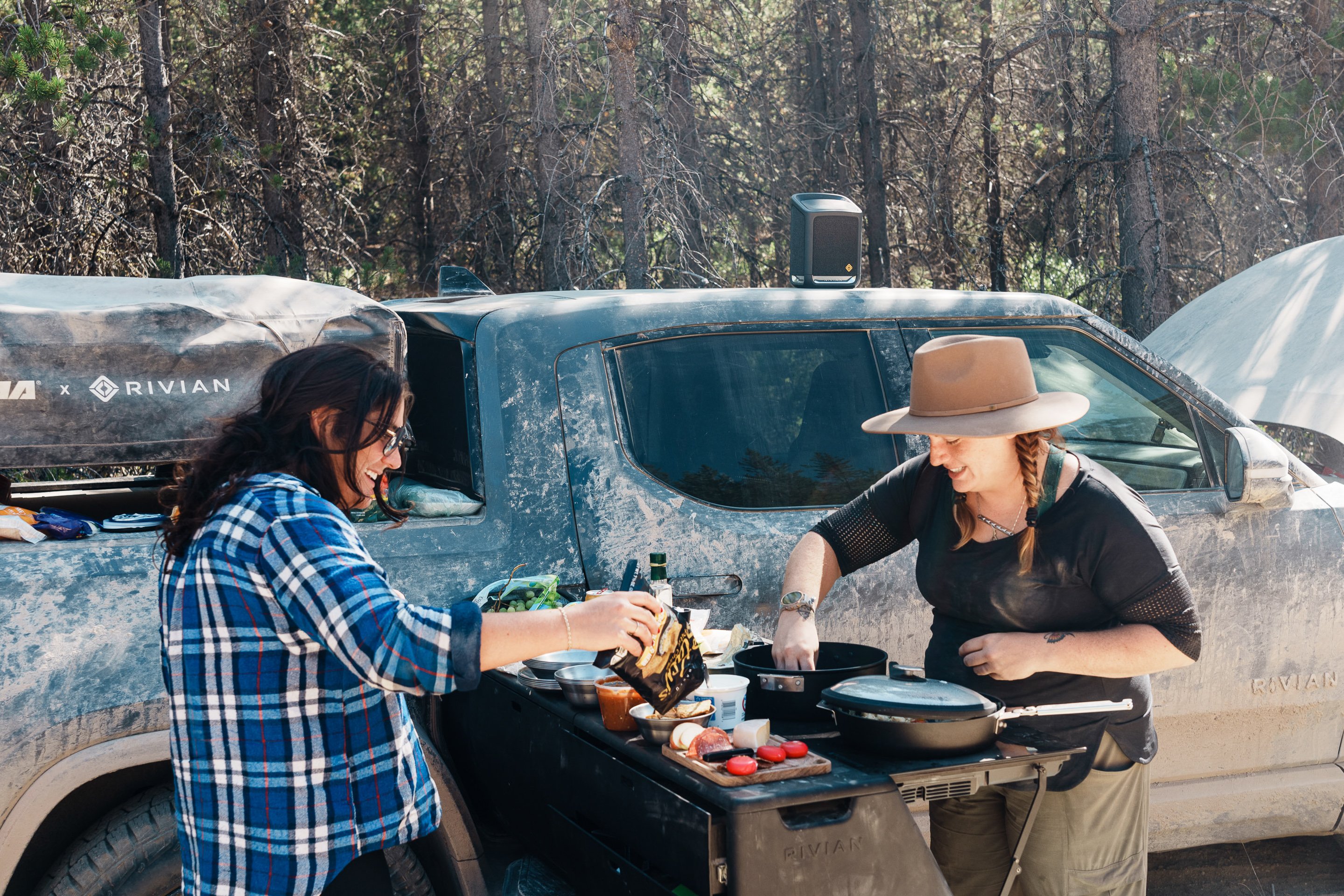 A pair of camping buddies having breakfast beside their Rivian electric truck. 