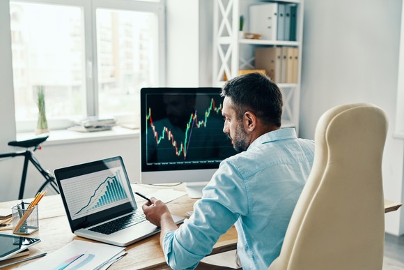 A person is looking at stock charts and other financial information on computers while sitting at a desk. 