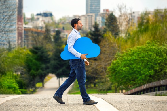 A person walks with a blue cutout of a cloud under their arm. 