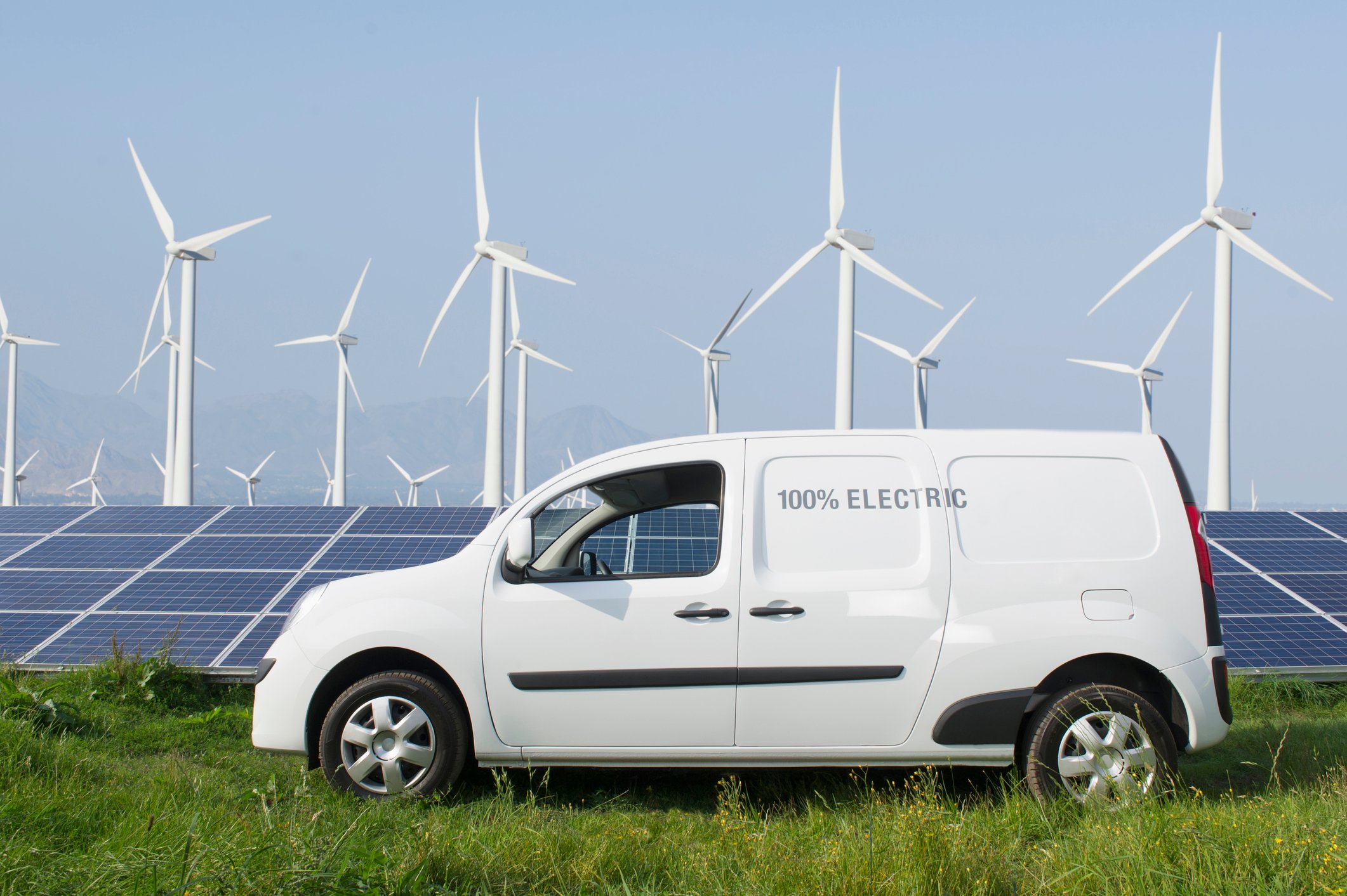 An electric van in front of wind turbines and solar panels.