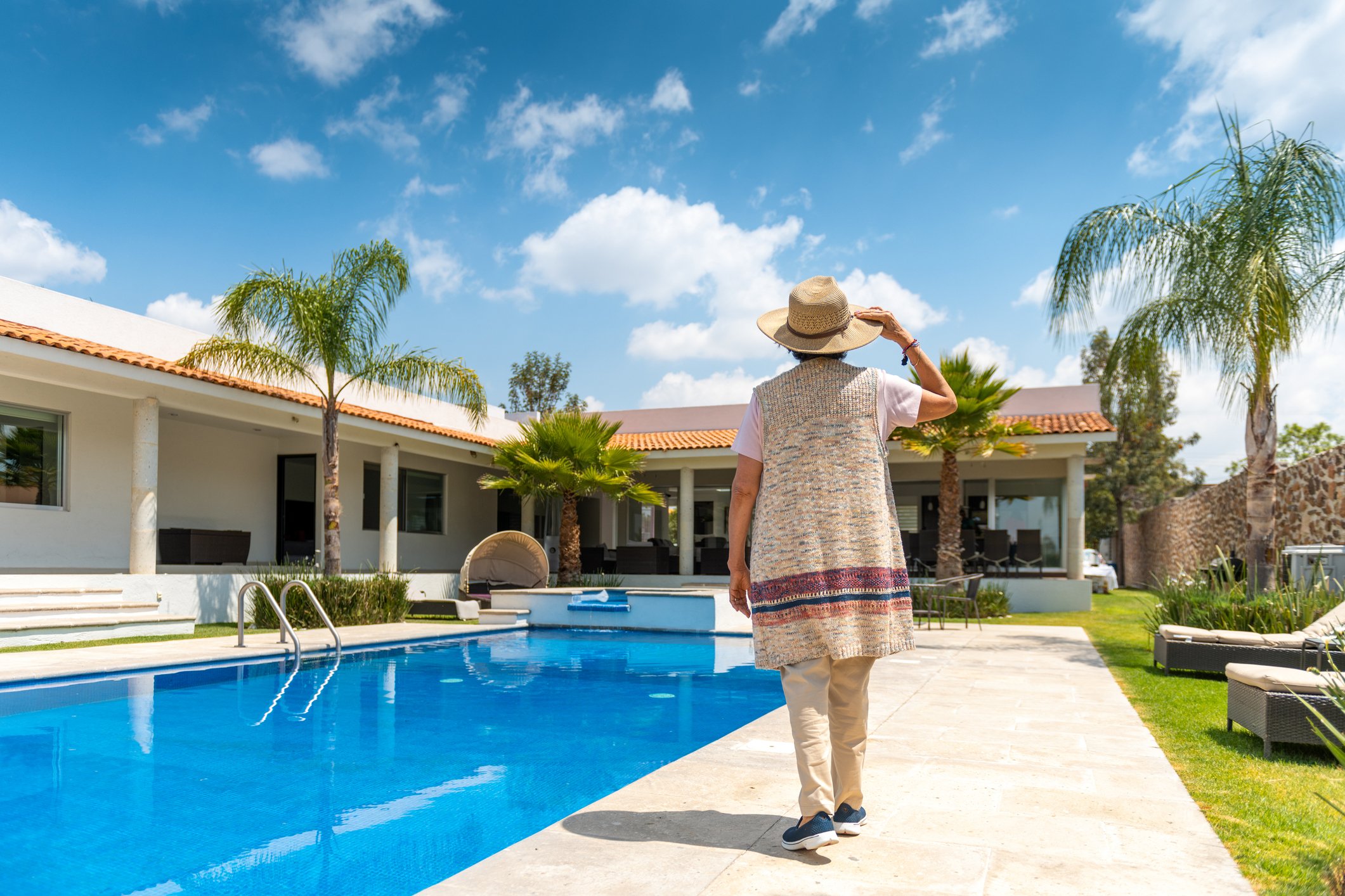 Person in a sun hat walking by a home swimming pool. 