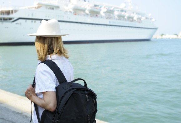 A person with a backpack looks at a docked cruise ship.