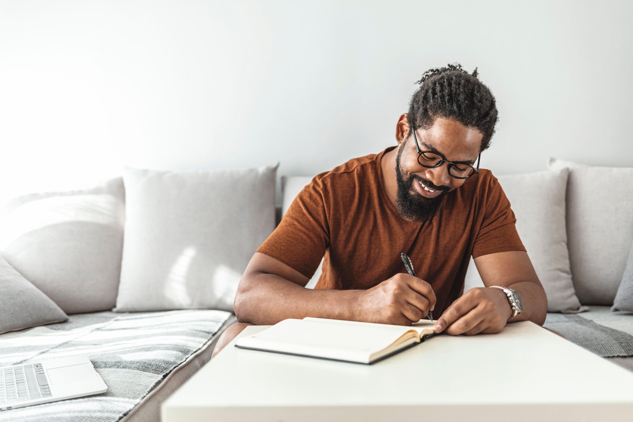 A person sits at a coffee table, writing in a notebook.