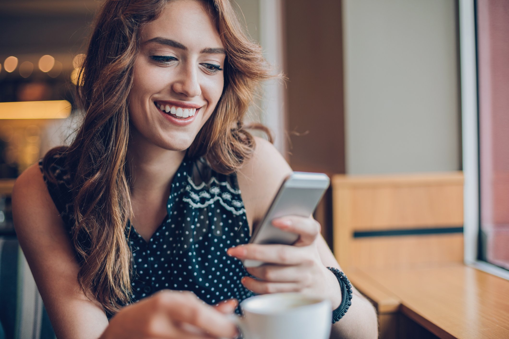 Woman smiles at her phone in a coffeeshop. 