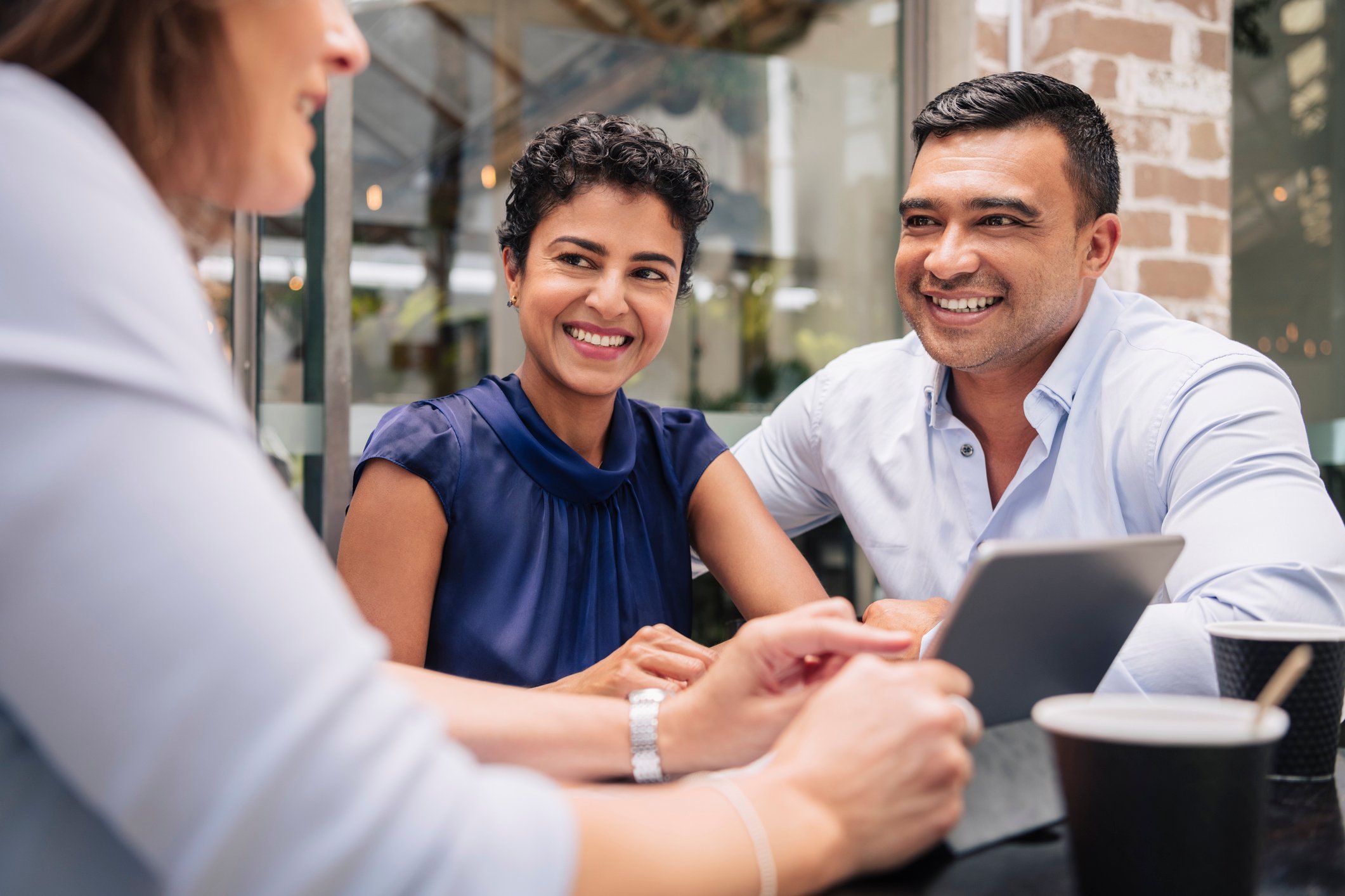 Three people sit at a table with a tablet.