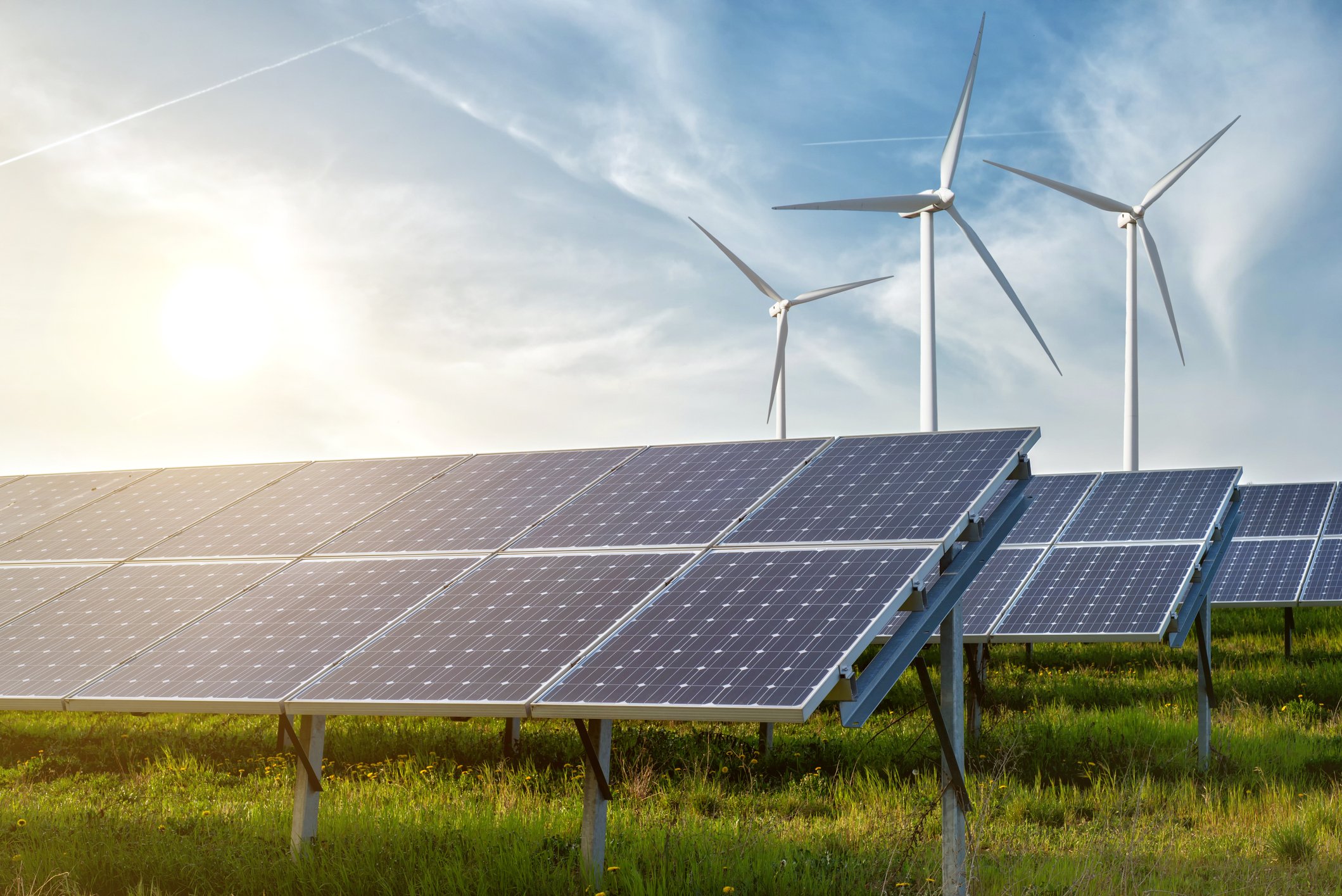 Solar farm in a field with wind turbines in the background. 