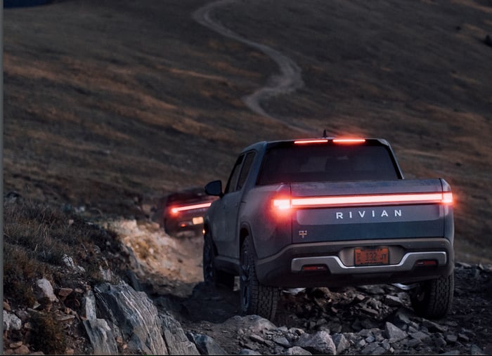 Two Rivian trucks heading up mountain trail at dusk.