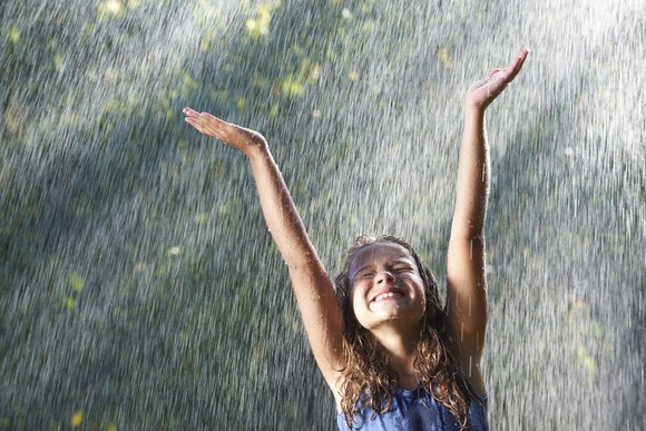 A smiling person playing in the rain.